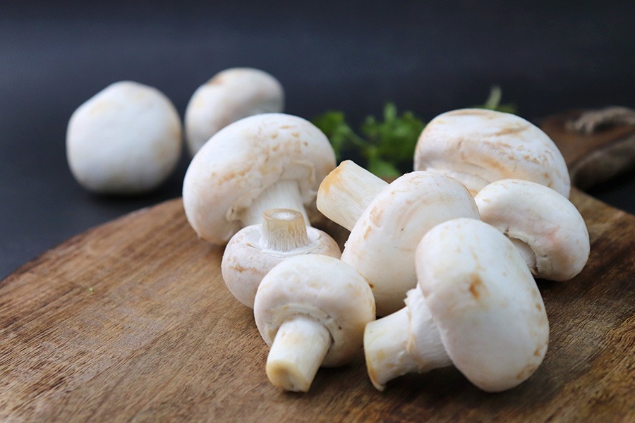 Fresh mushrooms on a wooden chopping block, neatly arranged and ready for cooking, highlighting the key ingredients in mushroom recipes.